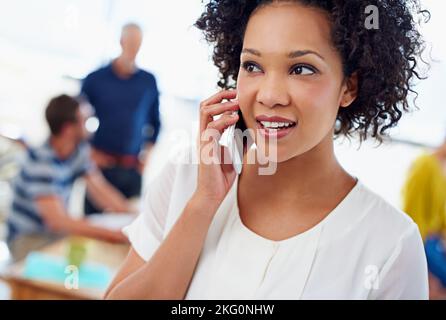 Elle s'assure que ses est constamment informé. Portrait rogné d'une femme parlant au téléphone avec des collègues en arrière-plan. Banque D'Images