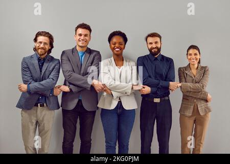 Portrait d'un groupe souriant de divers hommes d'affaires multiraciaux debout dans une rangée tenant les mains. Banque D'Images