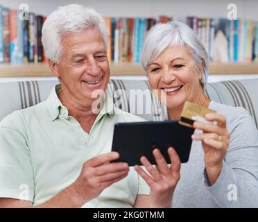 Il n'est plus nécessaire d'aller au centre commercial. Un couple senior heureux faisant des achats en ligne sur une tablette numérique. Banque D'Images