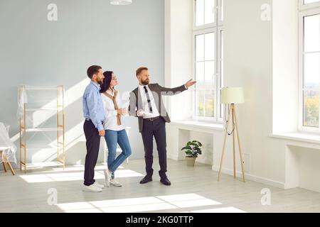 Agent immobilier jeune homme montrant nouveau grand appartement moderne pour couple d'acheteurs ou de locataires. Banque D'Images