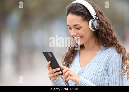 Une bonne femme marche à écouter de la musique en regardant le téléphone dans la rue Banque D'Images