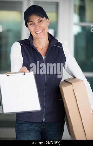 coursier féminin avec colis tenant le presse-papiers vers l'avant pour une signature Banque D'Images