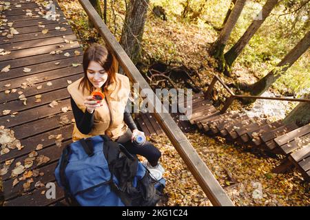 Une femme en voyage de randonnée boit une boisson chaude de la coupe thermos dans la forêt d'automne Banque D'Images