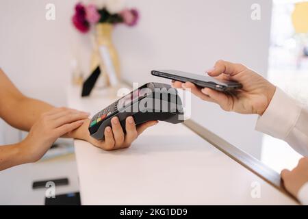 Les femmes paient pour les procédures dans le studio de beauté. Gros plan de la femme payer par téléphone et mettre au terminal. Le caissier tient le lecteur de carte de crédit Banque D'Images