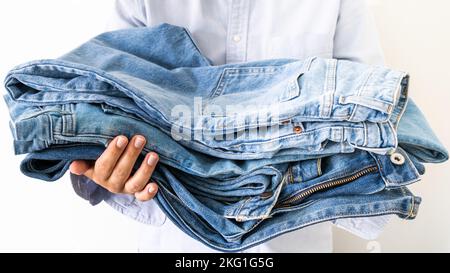 Pile de jeans dans les mains du vendeur sur fond clair Banque D'Images