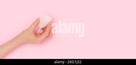 Bannière avec une main femelle tient une tasse blanche sur fond rose. Concept minimal avec place pour le texte. Mise au point sélective. Banque D'Images