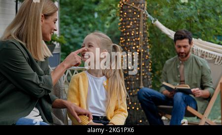 Mère caucasienne parlant rire avec fille drôle touchant le nez de bébé petite fille en train de courir embrassant papa par le cou cuddling à la lecture de père barbu Banque D'Images