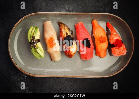 Assortiment de sushis Nigiri sur une assiette, sur béton foncé. Vue de dessus Banque D'Images