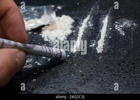 Utilisation à partir d'un sac en plastique de cocaïne à travers un tube respiratoire d'une facture de cent dollars, sur fond noir, gros plan Banque D'Images