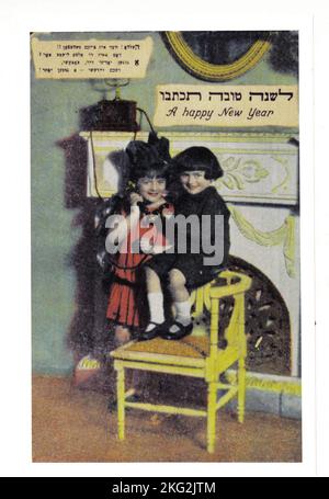 Une carte du nouvel an juif du début du 20th siècle, principalement en yiddish, mais aussi en hébreu et en anglais. Elle dépeint deux jeunes enfants qui prolongent leurs salutations sur un téléphone à l'ancienne, une invention relativement nouvelle pour la maison. Banque D'Images