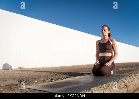 Femme s'agenouillant sur son tapis d'exercice extérieur au soleil Banque D'Images