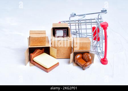 Boîtes de livraison compactes non emballées avec des figurines de meubles miniatures par un petit chariot à pousser isolé sur fond blanc. Acheter des meubles pour un nouvel appart Banque D'Images