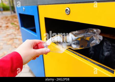 Jeter à la main une bouteille en plastique dans une poubelle de couleur dans le parc local. Concept de collecte et de recyclage des déchets. Banque D'Images