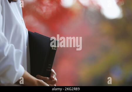 Un chrétien tenant la Sainte Bible et prêchant l'évangile de Jésus-Christ et une scène de rue d'automne avec des feuilles rouges Banque D'Images