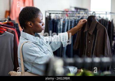 Portrait de la jeune femme noire à vue latérale regardant les vêtements dans le magasin d'occasion Banque D'Images