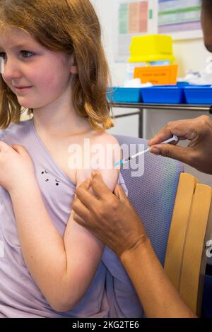 Une jeune fille de 8 ans reçoit le vaccin d'ARNm Comirnarty 10 COVID-19 pour l'inoculer contre l'infection par le delta d'Omicron ou d'autres variantes existantes du coronavirus. L'infirmière administre l'injection au centre de santé local de Teddington. ROYAUME-UNI. (132). L'enfant qui reçoit le vaccin est un modèle libéré. Banque D'Images