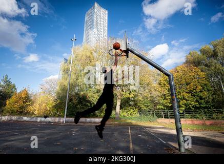 Un jeune homme saute en jouant au basket-ball Hulme Park à l'ombre de la tour sud du nouveau développement du centre-ville. Manchester Royaume-Uni crédit photo garyroberts/monde Banque D'Images