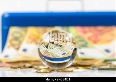 billets et pièces en euros couchés sur la table et collés de la caisse bleue avec réflexion dans la boule de verre Banque D'Images