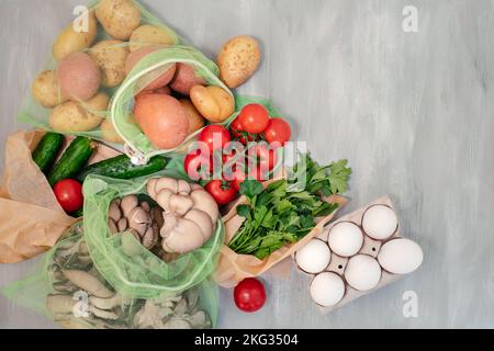 Légumes dans des sacs en filet réutilisables sur fond de bois gris, vue du dessus. Concept écologique et sans gaspillage Banque D'Images