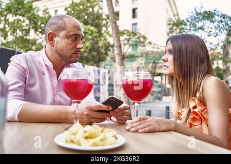 Vue latérale d'un couple aimant assis à table avec des cocktails en verre et regardant les uns les autres tout en appréciant la date dans le patio du café d'été Banque D'Images