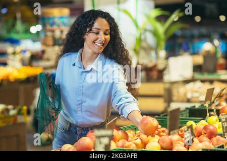 Femme heureuse acheteuse au supermarché, femme latino-américaine achète des pommes, des fruits et des légumes, met dans un sac écologique. Banque D'Images