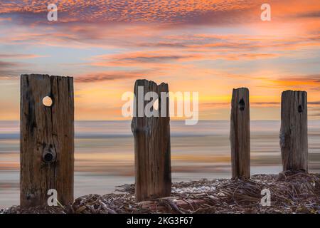 Des poteaux abîmés et un magnifique ciel coloré à l'aube sur la belle plage de West Wittering. Banque D'Images