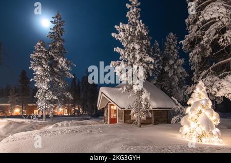 Scène extérieure d'hiver et de Noël avec cabine en bois. Paysage forestier d'hiver en pleine lune, Finlande, Laponie. Banque D'Images