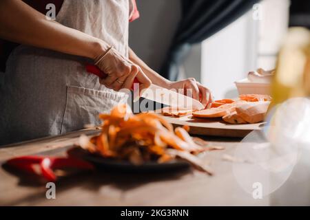 Jeune femme coupant de la patate douce tout en cuisinant dans la cuisine à la maison Banque D'Images