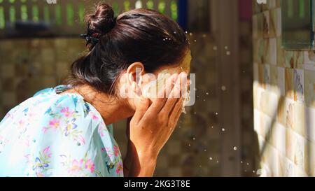 Belle femme est de laver le masque facial dans la salle de bains après avoir appliqué le masque facial. Fille pulvérisant de l'eau sur son visage debout devant le miroir à la maison. Boue Banque D'Images