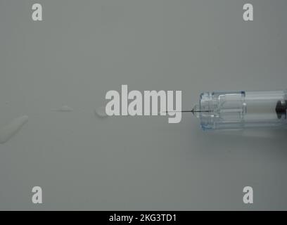 Un gros plan d'une seringue remplie d'un liquide avec des gouttes à l'extrémité de l'aiguille sur un fond gris. Banque D'Images