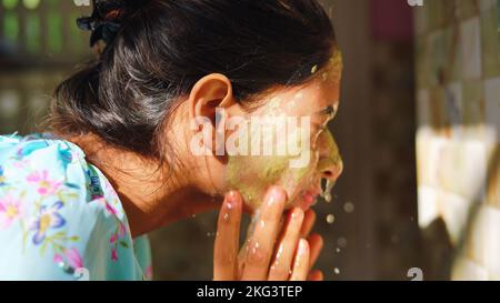 Belle femme est de laver le masque facial dans la salle de bains après avoir appliqué le masque facial. Fille pulvérisant de l'eau sur son visage debout devant le miroir à la maison. Boue Banque D'Images