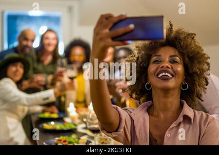 femme afro-américaine adulte prenant le selfie avec ses amis, dîner végétalien avec des personnes de divers âges et diverses, femme utiliser l'application mobile pour photographier Banque D'Images