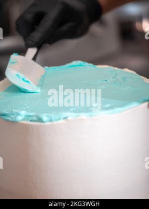cake designer lissant un gâteau blanc givré avec de la crème de beurre bleu turquoise clair avec une spatule Banque D'Images