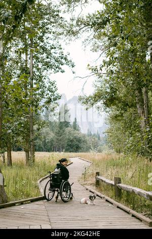 Femme en fauteuil roulant voyageant à travers Yosemite avec un chien Banque D'Images
