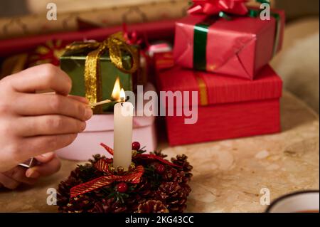 Gros plan des mains d'une femme utilisant des allumettes, éclairant une bougie décorative debout près des cadeaux de Noël sur une table en marbre Banque D'Images