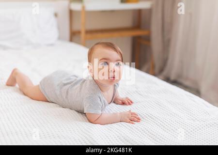 Concept de garde d'enfants. Portrait d'un bébé mignon portant un body allongé sur des feuilles blanches à la maison, espace libre Banque D'Images