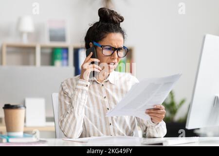 Stress commercial. Femme d'affaires en colère ayant des problèmes, parlant sur un smartphone et tenant des papiers, arguant avec le client Banque D'Images