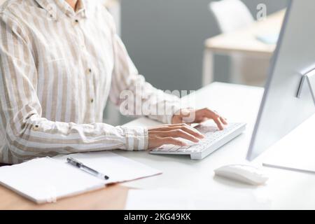 Employée féminine non reconnaissable travaillant sur un ordinateur au bureau, image rognée d'une femme tapée au clavier Banque D'Images