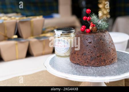 Un pudding de Noël frais traditionnel avec un pot de beurre de Brandy. Le pudding est décoré de baies festives et d'une branche de feuilles de pin dépolies Banque D'Images