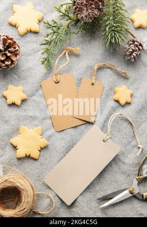 Étiquettes cadeau vierges avec branche de pin et biscuits de Noël sur fond textile. Le concept de la préparation des vacances de Noël. Pose à plat Banque D'Images