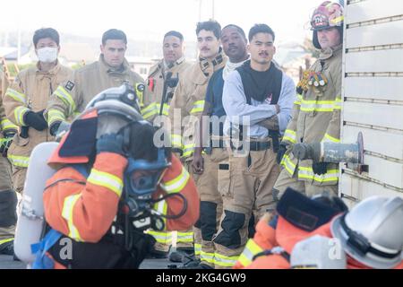 Des aviateurs de lutte contre les incendies de l'escadron du génie civil 374th regardent les pompiers de la Force aérienne japonaise d'autodéfense montrer comment combattre un incendie structurel lors d'un entraînement bilatéral à la base aérienne de Yokota, au Japon, le 28 octobre 2022. Les aviateurs de pompiers de la SCÉ 374 et de la JASDF ont démontré des techniques de lutte contre l'incendie les uns pour les autres et ont comparé des méthodes, des matériaux et des tactiques. Banque D'Images