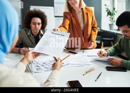 Les mains de jeunes femmes musulmanes qui prennent le test de grammaire sont passées par un professeur de langue anglaise avant le travail individuel Banque D'Images
