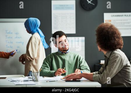 Homme du Moyen-Orient confiant regardant le camarade de classe et l'écoutant en leçon contre une jeune étudiante musulmane en hijab bleu Banque D'Images