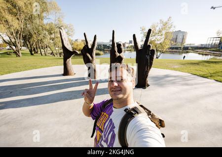 Lviv, Ukraine - 09 octobre 2022: Touriste avec sac à dos faisant selfie contre la sculpture métallique de quatre mains à la ville de Lviv, Ukraine. Banque D'Images