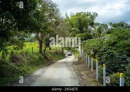 Filandia, Quindio, Colombie - 6 juin 2022: Une voiture passant par une route de terre entourée d'un grand nombre d'arbres et de plantes, et une clôture de fil Banque D'Images