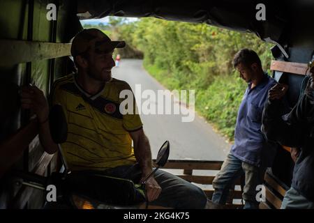 Filandia, Quindio, Colombie - 6 juin 2022: Jeune homme caucasien avec sa moto se tient sur un tuyau dans l'arrière de la voiture avec d'autres passagers Banque D'Images