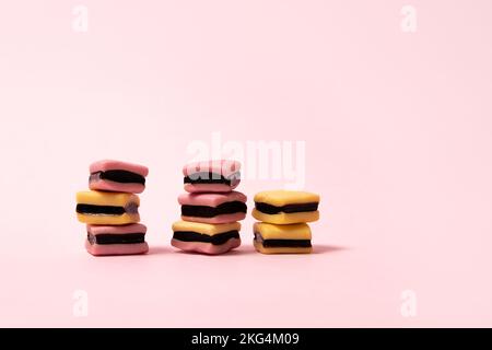 Piles de bonbons à la réglisse rose et jaune sur fond rose Banque D'Images