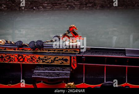 Un superbe ornement en laiton de cheval d'eau sur le côté d'une gondole en bois avec la rougeur de la peinture reflétée dans le dessin. Banque D'Images