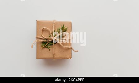 Boîte cadeau en carton Kraft attachée avec une corde de jute rugueuse sur fond de bois gris avec des branches d'arbre de Noël et des décorations de Noël Banque D'Images