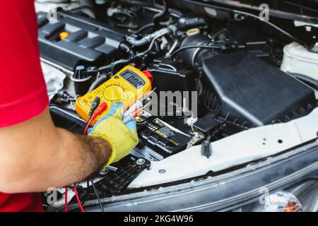 Un mécanicien possède un multimètre numérique pour vérifier le système électrique de la voiture, concept d'entretien automatique Banque D'Images